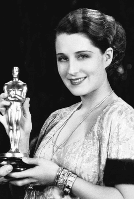 Norma Shearer holding an Academy Award while wearing jewelry