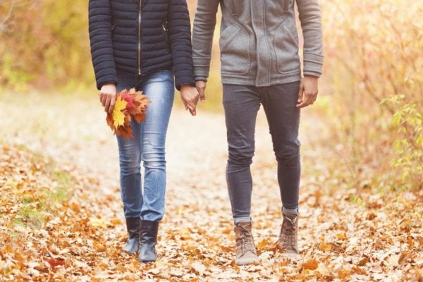 Couple with bunch of leaves walking in autumn park